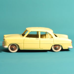 Può includere: Un'auto giocattolo gialla con tetto bianco e ruote nere. L'auto è un modello vintage e ha un design classico.