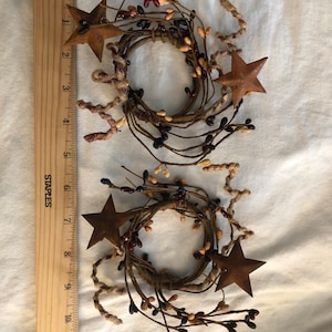 May include: Two rustic brown twig candle rings with small brown, black, and cream berries and two rusty metal star accents.