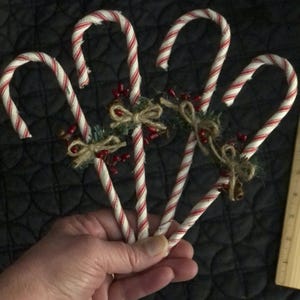 May include: Three red and white striped candy cane ornaments with green and brown burlap bows and red berries.