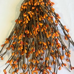 May include: A bundle of artificial berries with orange and red hues. The berries are small and oval-shaped, clustered on thin, brown stems. The stems are arranged in a cascading pattern, creating a full and textured appearance, perfect for fall decor.