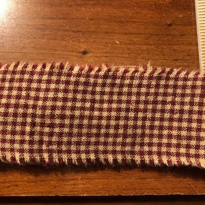 K&ouml;nnte beinhalten: Rotes und cremefarbenes Gingham-Gewebe mit ausgefransten Kanten.