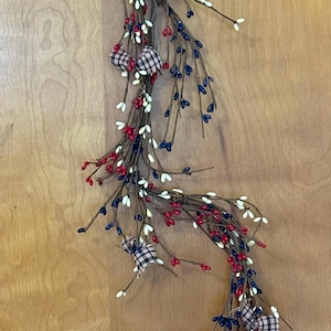 May include: A decorative garland featuring red, white, and blue berries on brown stems, accented with plaid bows. This patriotic-themed garland is suitable for seasonal home decor and celebrations.