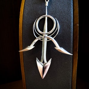 May include: A silver pendant necklace with a geometric design featuring a circle, a cross, and two curved lines. The pendant is attached to a silver chain.