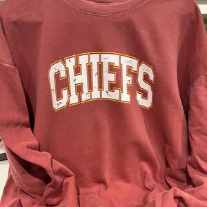 May include: A red long-sleeved sweatshirt with the word "CHIEFS" printed in white with a yellow outline.
