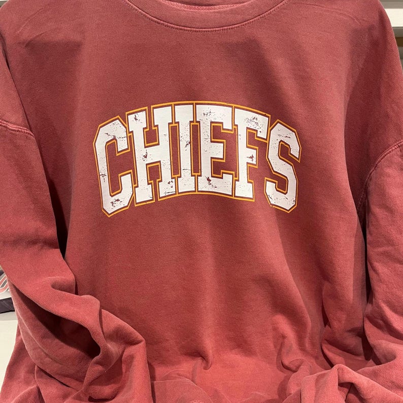 May include: A red long-sleeved sweatshirt with the word "CHIEFS" printed in white with a yellow outline.