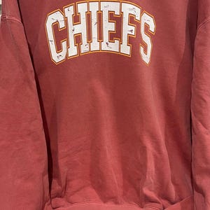 May include: A red sweatshirt with the word "CHIEFS" printed in white with a yellow outline.