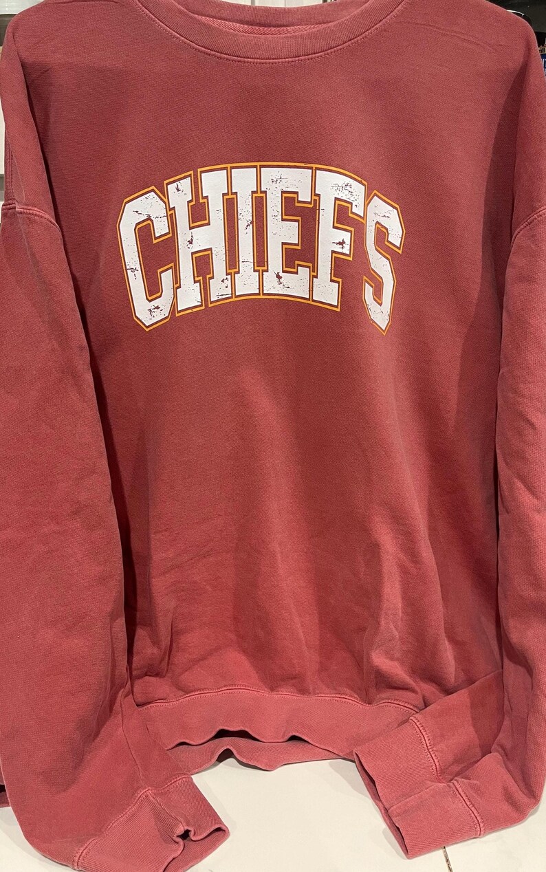 May include: A red sweatshirt with the word "CHIEFS" printed in white with a yellow outline.