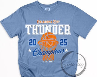 Może przedstawiać: Jasnoniebieska koszulka z napisem "Oklahoma City Thunder" i grafiką koszykówki. Koszulka wyświetla również "2025 Champions" i "Est. 2008" w kolorze białym i niebieskim. Koszulka ma okrągły dekolt.
