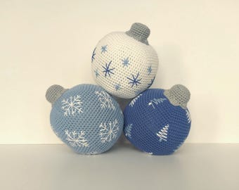 May include: Three crocheted Christmas ornaments in blue and white. The ornaments are shaped like balls and have different designs. One ornament has snowflakes, one has trees, and one has a snowflake pattern.