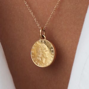 May include: A gold chain necklace with a gold coin pendant featuring a profile of a person with a laurel wreath. The coin has the text "REPUBLICA ITALIANA" around the edge.