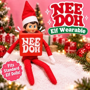 May include: A red square wearable accessory for an elf doll, featuring the white text "NEE DOH" on the front. The item is worn by a doll with a red hat and red clothing. Additional text in the image reads "NEE DOH Elf Wearable" and "Fits Standard Elf Dolls!"