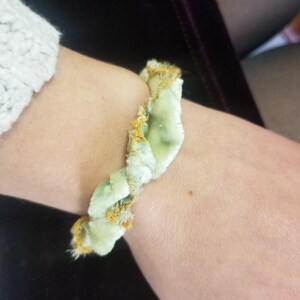 May include: A green and gold velvet bracelet with a twisted design.