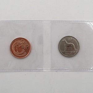 May include: Two vintage coins displayed in a clear plastic holder. One coin is copper-colored with an ornate design and the letters "NP". The other is silver-colored, featuring a greyhound and the word "Reul".