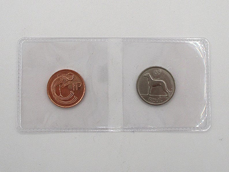 May include: Two vintage coins displayed in a clear plastic holder. One coin is copper-colored with an ornate design and the letters "NP". The other is silver-colored, featuring a greyhound and the word "Reul".
