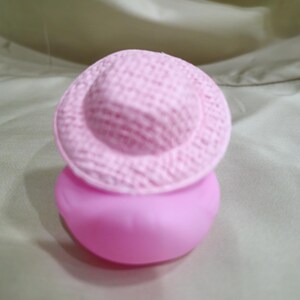 May include: A pink rubber bath toy shaped like a duck wearing a pink hat.