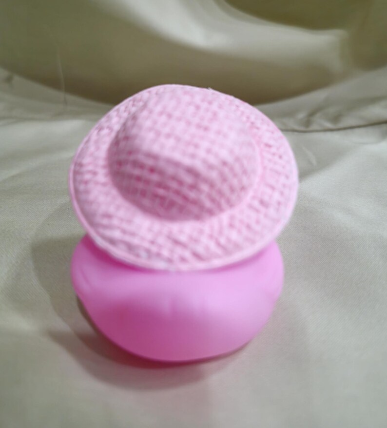 May include: A pink rubber bath toy shaped like a duck wearing a pink hat.