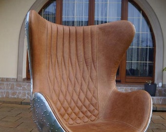 May include: A brown leather egg-shaped chair with a silver metal base and rivets. The chair is sitting on a patio.