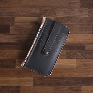 Peut inclure: Un portefeuille rectangulaire gris foncé doté d'une sangle verticale avec fermeture à bouton-pression et de multiples fentes pour cartes cousues. Le côté du portefeuille révèle une doublure en tissu à motifs avec une tirette de fermeture éclair.