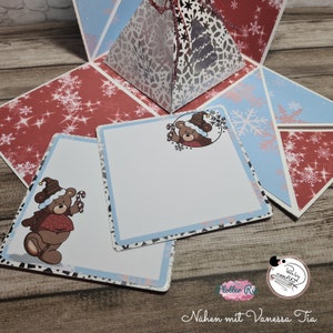 Puede incluir: Una caja de artesanía de papel roja y azul con una pirámide blanca en el centro. La pirámide tiene un diseño de copo de nieve y un oso con un bastón de caramelo en la boca. La caja tiene dos tarjetas en blanco con un diseño de oso en cada una.