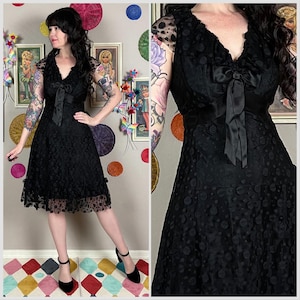 以下が含まれることがあります： Vネックとウエストにリボンが付いた黒のヴィンテージドレス。ドレスは水玉模様で、裾はフリルになっています。短い袖は、透け感のある水玉模様の生地で作られています。モデルは黒いハイヒールを履いています。