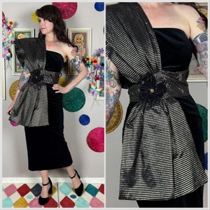 Puede incluir: Un vestido negro sin tirantes de terciopelo con un acento a rayas doradas y negras. El vestido presenta un cinturón decorativo con un adorno floral. El vestido se combina con tacones negros.