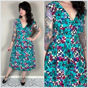 May include: A sleeveless knee-length dress featuring a vibrant floral pattern in shades of teal, magenta, and white against a black polka dot background. The dress has a V-neckline, a fitted waist, and a pleated skirt that falls below the knees.