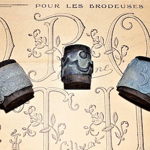 May include: Three vintage wooden printing blocks with intricate designs. The blocks are used for embroidery and feature floral and wave patterns. The blocks are on a paper background with the text "Pour les brodeuses".