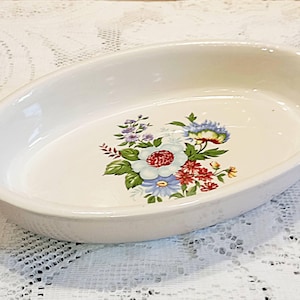 Op de afbeelding: Ovale, crèmekleurige keramische ovenschaal met handvatten. Een bloemenontwerp in rood, wit, blauw en paars siert het midden. Ideaal om te serveren of te bakken.