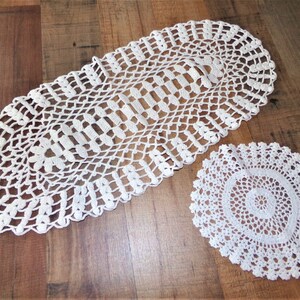 May include: Two white crocheted doilies, one oval and one round, on a wooden surface.