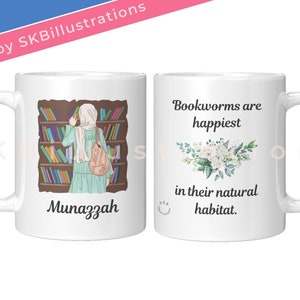 May include: White ceramic mug with a colorful illustration of a woman in a headscarf standing in front of a bookshelf. The text "Munazzah" is printed below the illustration. The other side of the mug has a floral design and the text "Bookworms are happiest in their natural habitat."