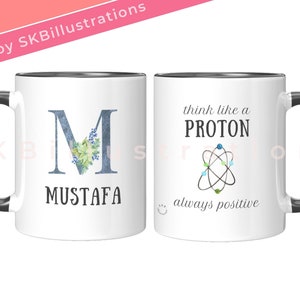 May include: White ceramic mug with a black rim and handle. One side features a blue letter "M" with floral accents and the name "MUSTAFA" below. The other side has the text "think like a PROTON" with a stylized atom graphic and the text "always positive" below.