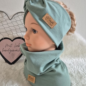 Könnte beinhalten: Ein türkisfarbenes Turban-Stirnband und ein passender Halsschmuck mit einem braunen Etikett mit der Aufschrift "Malkat by Anka".