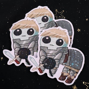May include: A cluster of stickers featuring a cartoon knight with a round head, large eyes, and blonde hair. The knight is clad in silver armor, holding a sword and shield. The background is black with gold star accents.