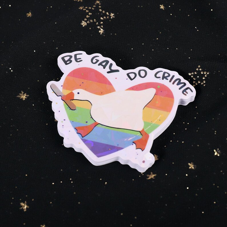 A sticker with a goose holding a knife on top of a rainbow heart, holding a knife in it's beak. The top says "Be Gay Do Crime"