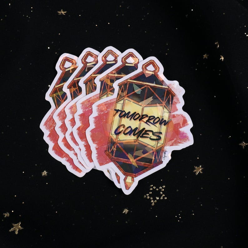 The Holographic lumina converter sticker with the text "Tomorrow Comes" on top. Behind the keychain is a red paint swipe.