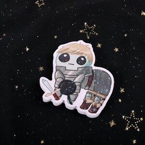 A holographic sticker Of Laios Touden  of Dungeon Meshi / Delicious in dungeon imagined as the yippee / Autism Creature. The sticker is on a black background with gold glitter.