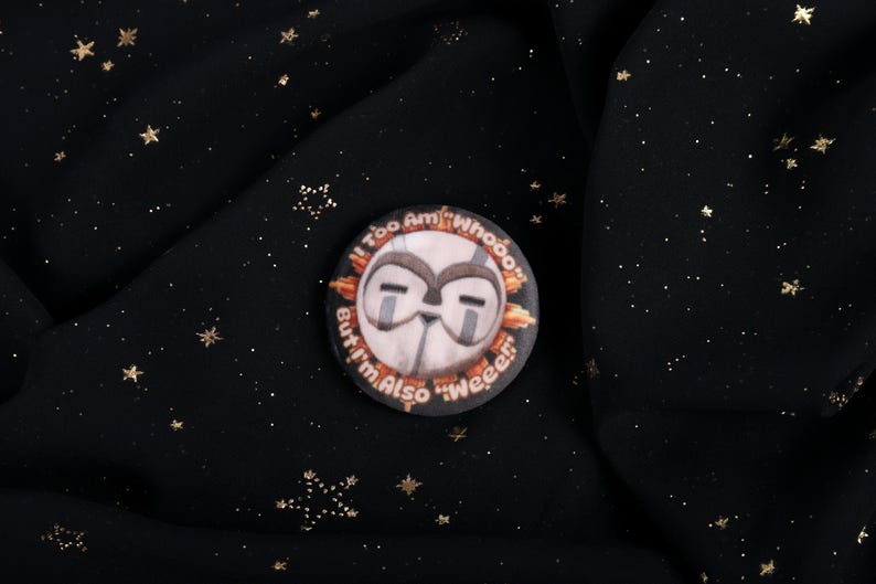 A squishy plush pin of Esquie from Expedition 33- It features Esquie's head from Clair Obscur Expedition 33 featuring the text: "I am too "Whooo" but I am also "Wheee"