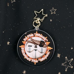 The Back of the Esquie Keychain. It features Esquie's head from Clair Obscur Expedition 33 featuring the text: "So the "Wheee" balances the "Whooo". He has the Expedition 33 Arm Band that Verso Gave him on his head.