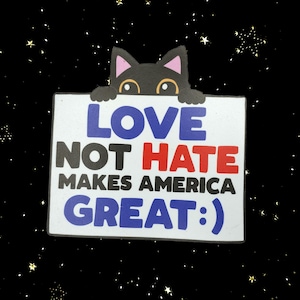 以下が含まれることがあります： 「LOVE NOT HATE MAKES AMERICA GREAT :)」の文字が青、赤、黒で書かれた白い看板を覗き込む黒猫。背景は黒で、白と黄色の星が散りばめられています。