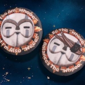 Puede incluir: Dos botones redondos con temática de búho y texto. Un botón dice "I Too Am 'Whooo' But I'm Also 'Weeee!'" El otro dice "So The 'Wheeee' Balances The 'Whooo'." Los botones tienen una cara de búho blanca con detalles grises.