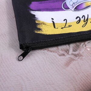 Puede incluir: Bolsa negra con cremallera con un dise&ntilde;o colorido que presenta una taza de t&eacute; y el texto "i love the tea!". El dise&ntilde;o incluye colores morado, blanco y amarillo. La bolsa tiene una cremallera negra y un tirador negro.