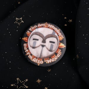 A squishy plush pin of Esquie from Expedition 33- It features Esquie's head from Clair Obscur Expedition 33 featuring the text: "I am too "Whooo" but I am also "Wheee"