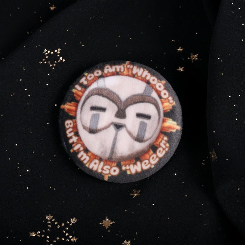 A squishy plush pin of Esquie from Expedition 33- It features Esquie's head from Clair Obscur Expedition 33 featuring the text: "I am too "Whooo" but I am also "Wheee"