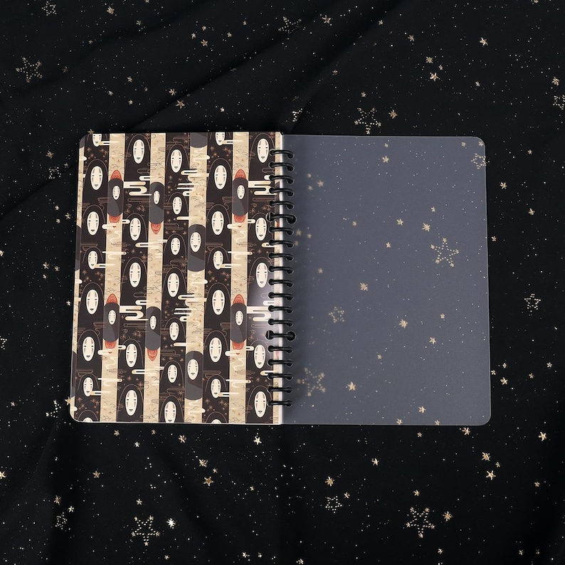 Puede incluir: Un cuaderno de espiral con un patr&oacute;n en blanco y negro de Sin Cara de la pel&iacute;cula El viaje de Chihiro. El cuaderno tiene una cubierta de pl&aacute;stico transparente.