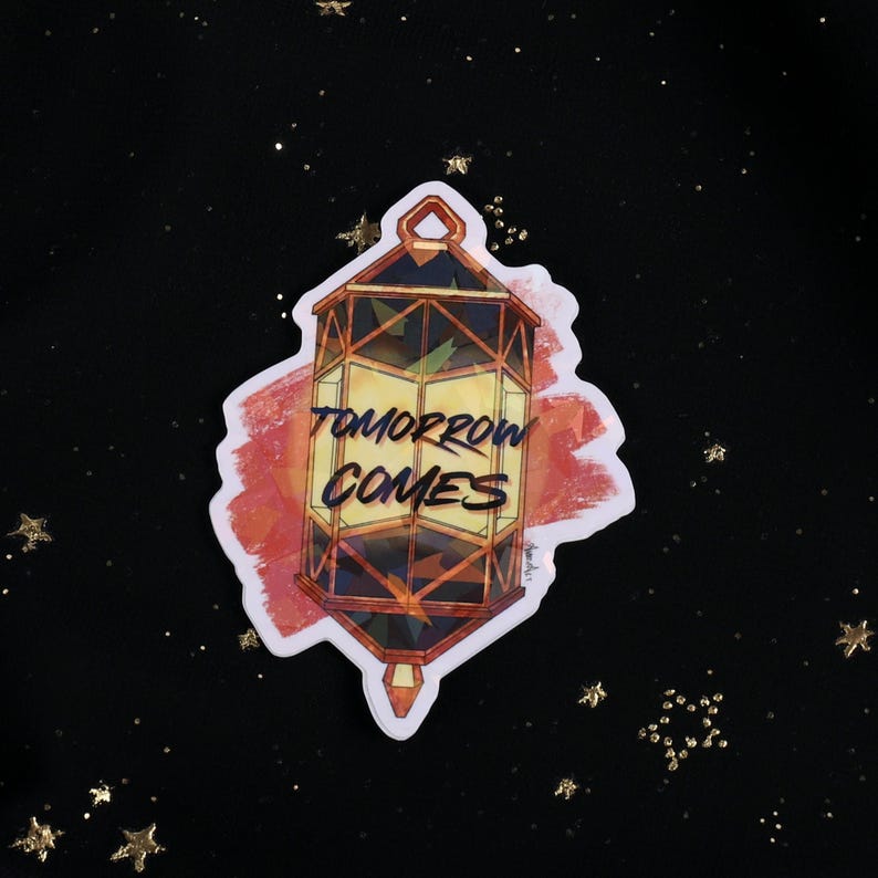 The Holographic lumina converter sticker with the text "Tomorrow Comes" on top. Behind the keychain is a red paint swipe.