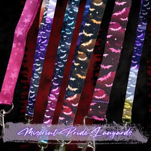 May include: A collection of lanyards with various patterns, including stars and bats, in shades of pink, purple, blue, and black. Each lanyard has a silver-colored clasp. The text "Misprint Pride Lanyards" is visible at the bottom.