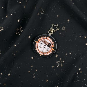 The Back of the Esquie Keychain. It features Esquie's head from Clair Obscur Expedition 33 featuring the text: "So the "Wheee" balances the "Whooo". He has the Expedition 33 Arm Band that Verso Gave him on his head.