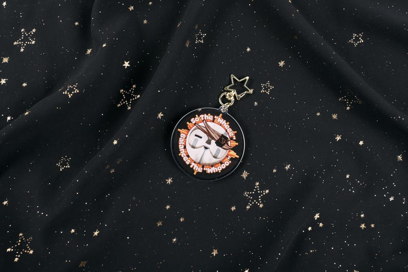 The Back of the Esquie Keychain. It features Esquie's head from Clair Obscur Expedition 33 featuring the text: "So the "Wheee" balances the "Whooo". He has the Expedition 33 Arm Band that Verso Gave him on his head.