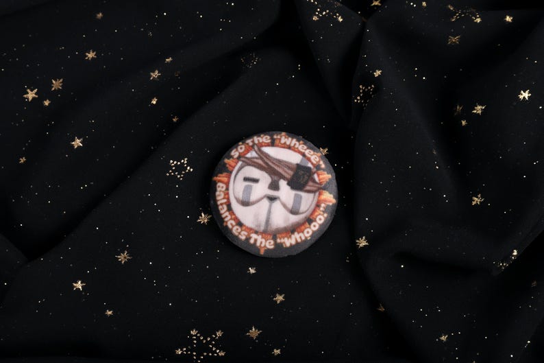 A Squishy Plush pin of Esquie from Expedition 33-  It features Esquie's head from Clair Obscur Expedition 33 featuring the text: "So the "Wheee" balances the "Whooo". He has the Expedition 33 Arm Band that Verso Gave him on his head.