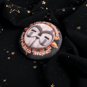 A squishy plush pin of Esquie from Expedition 33- It features Esquie's head from Clair Obscur Expedition 33 featuring the text: "I am too "Whooo" but I am also "Wheee"